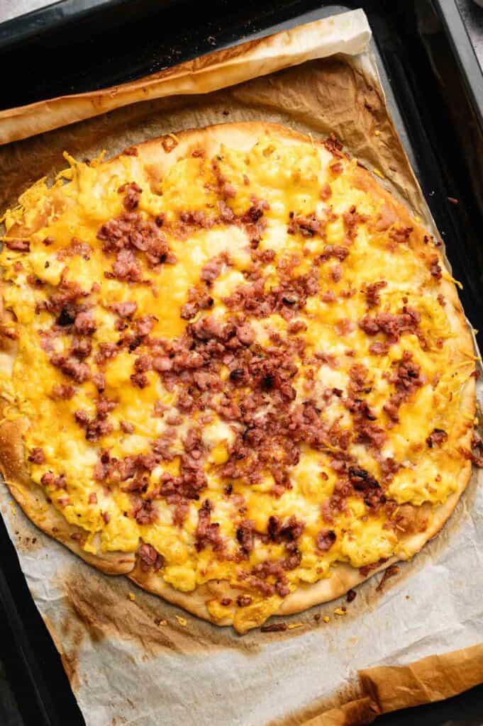 A delicious Breakfast Pizza topped with scrambled eggs, cheese, and crumbled bacon, baked to perfection on a parchment-lined baking sheet.