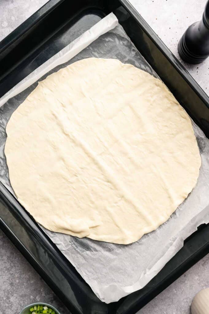 Pizza dough stretched on a baking sheet before pre-baking