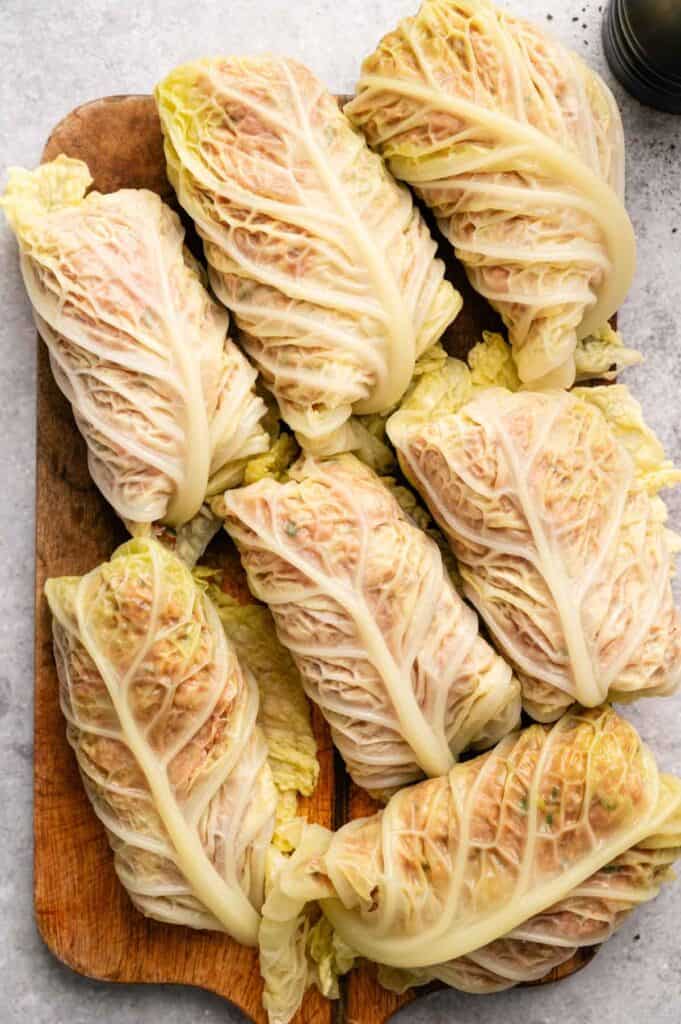 Seven savory Cabbage Rolls filled with a seasoned meat mixture are arranged on a wooden cutting board, highlighting the delicate veined texture of the cabbage leaves.