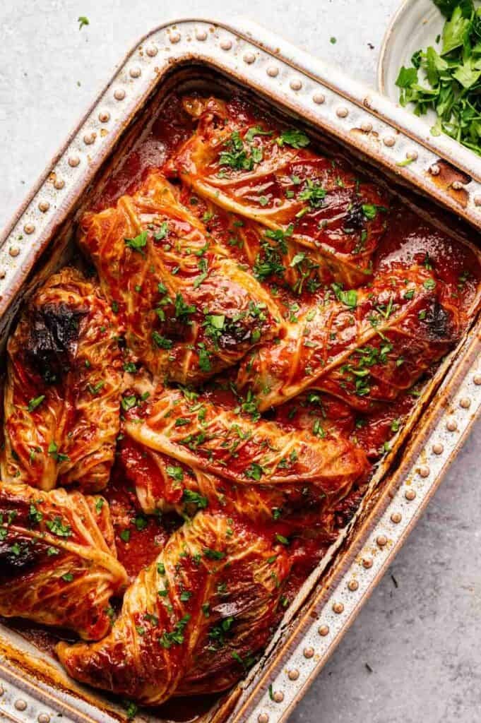 Cabbage Rolls filled with a savory mixture, baked to perfection and topped with tomato sauce and chopped parsley, arranged neatly in a rectangular baking dish.