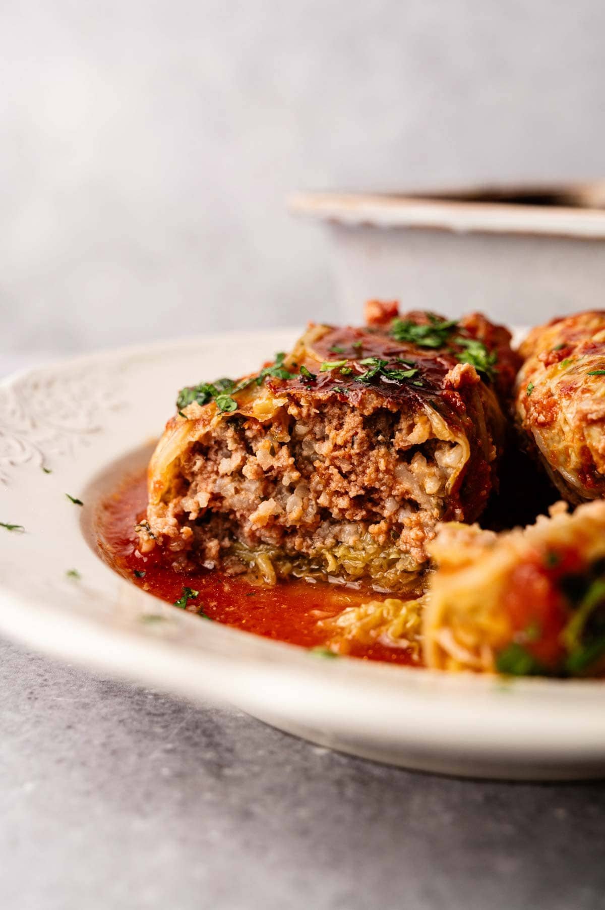A close-up of delicious Cabbage Rolls cut open to reveal a savory ground meat and rice filling, served with tomato sauce on a white plate.