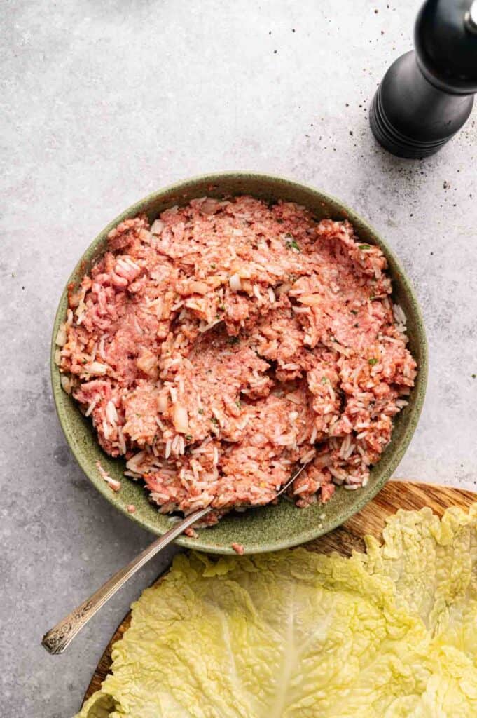 Ground beef and rice filling mixed in a bowl next to a cabbage leaf
