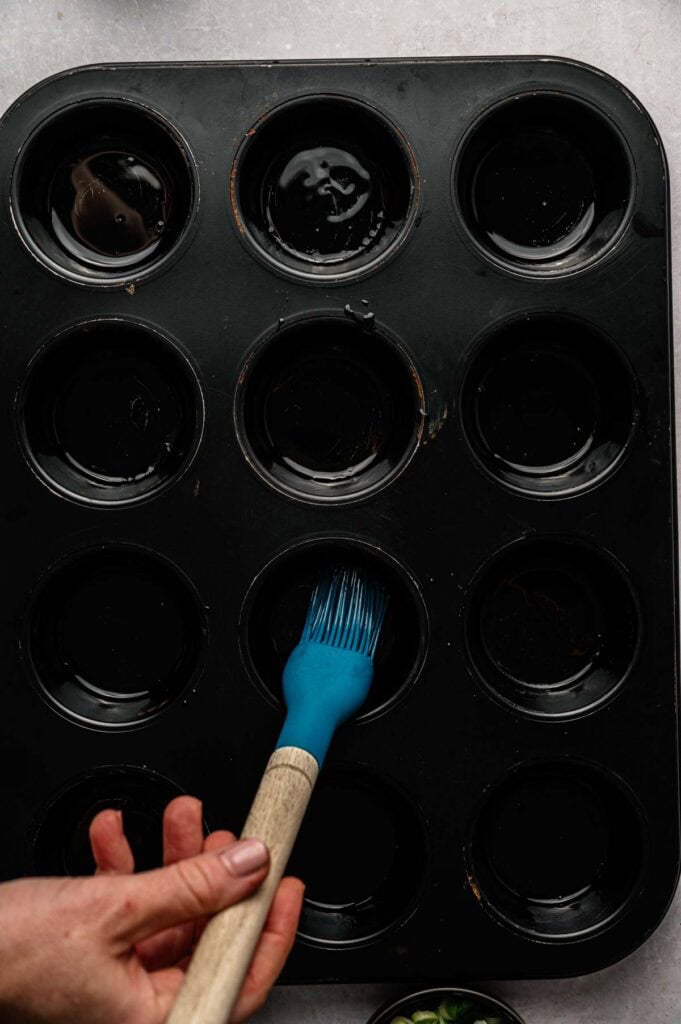 Hand oiling a nonstick muffin pan with a pastry brush before adding rice