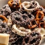A bowl of chocolate covered pretzels is coated in white and dark chocolate, then topped with chocolate sprinkles and shredded coconut.
