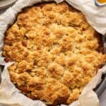 A round baking pan lined with parchment paper holds a golden-brown, crumbly Irish Apple Cake dessert fresh from the oven.