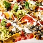 Close-up of Sheet Pan Nachos loaded with ground beef, black beans, guacamole, salsa, sour cream, melted cheese, and fresh cilantro.