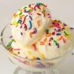 Two scoops of Vanilla Ninja Creami Ice Cream in a glass bowl, topped with colorful rainbow sprinkles, against a plain background.