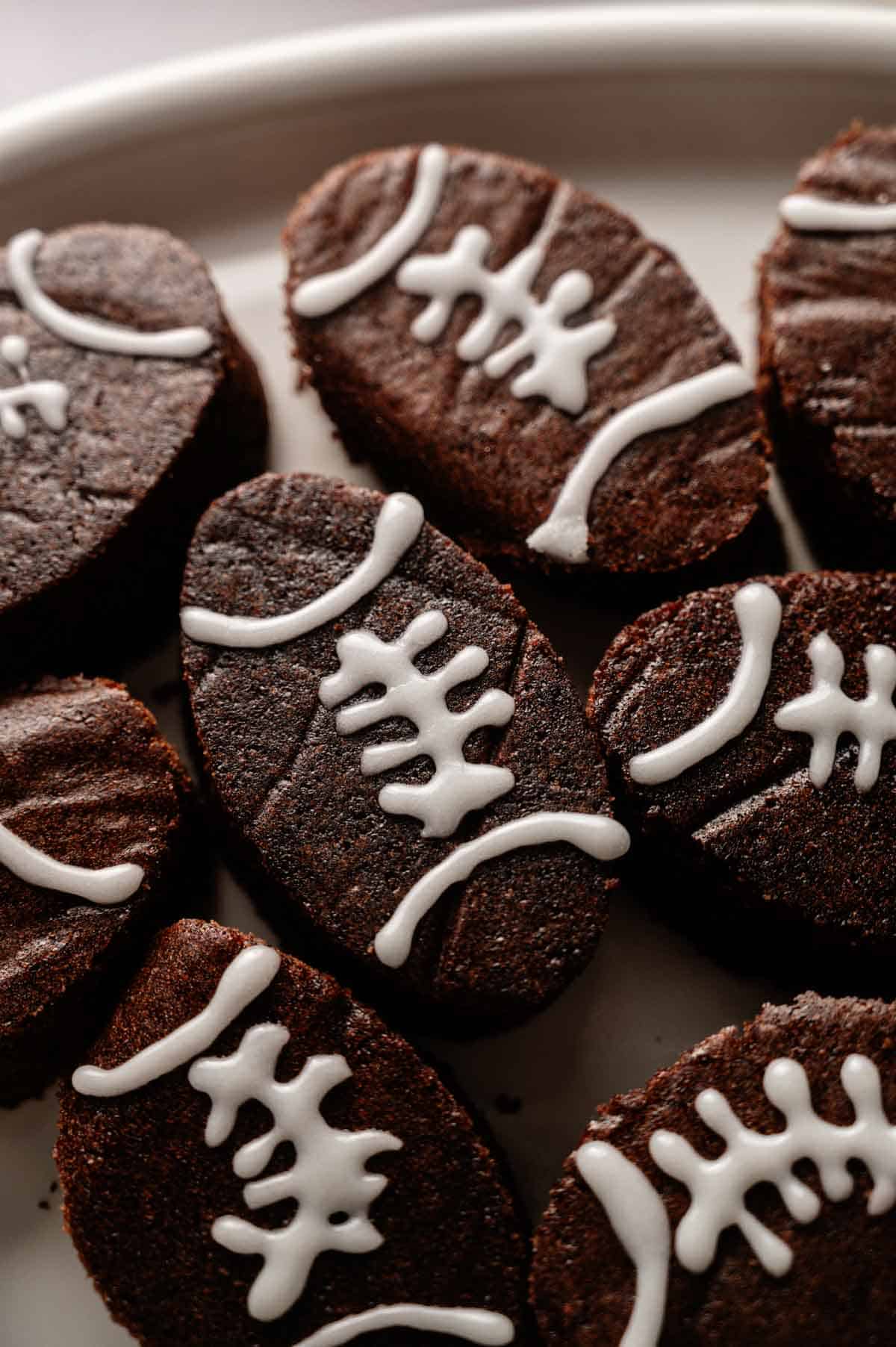 Football Shaped Brownies decorated with white icing to resemble football laces, arranged neatly on a white plate.