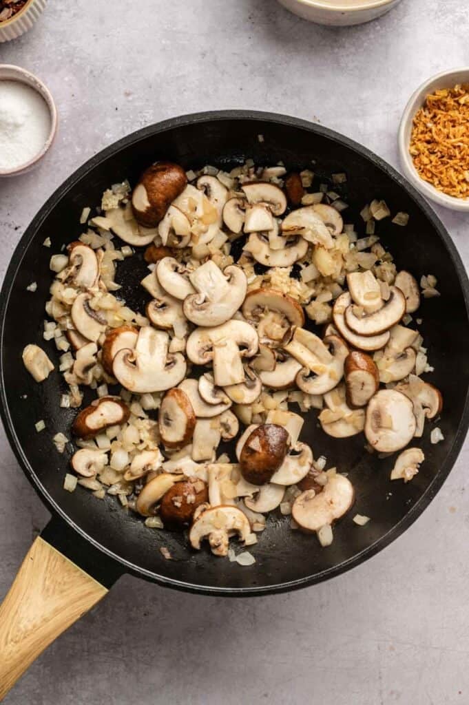 Sliced mushrooms cooking with softened onions in a cast iron skillet