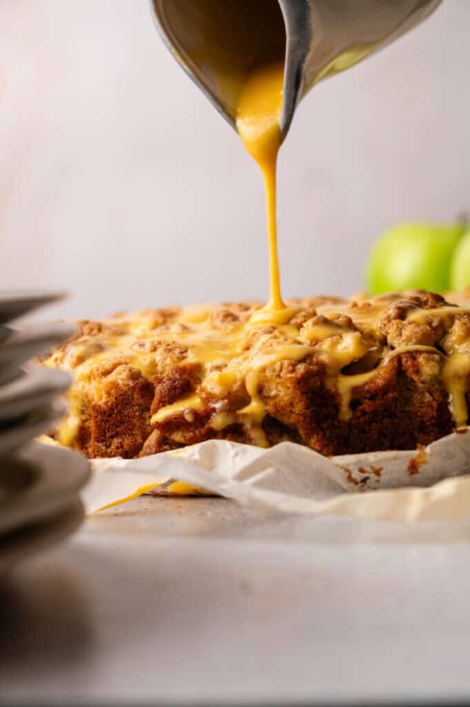 Close-up of golden custard drizzling over baked apple cake with streusel topping