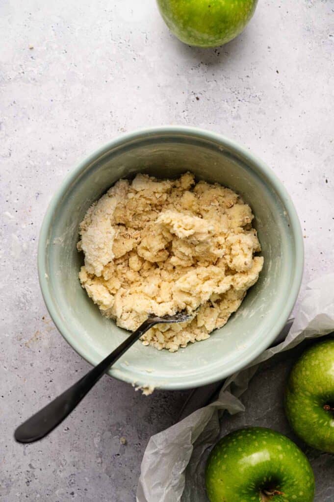 Overhead view of buttery oat streusel topping with fresh green apples nearby