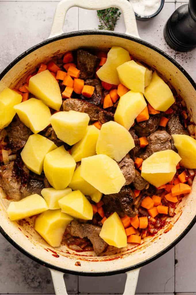 Overhead view of raw potato chunks layered over beef and diced carrots