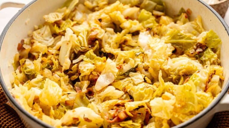 Chopped cooked cabbage with browned edges in a large white pot.