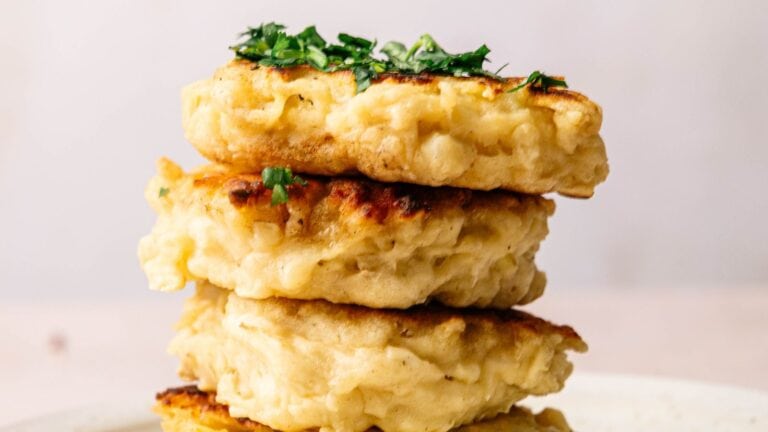 Three golden-brown fritters stacked on a plate, topped with chopped green herbs.
