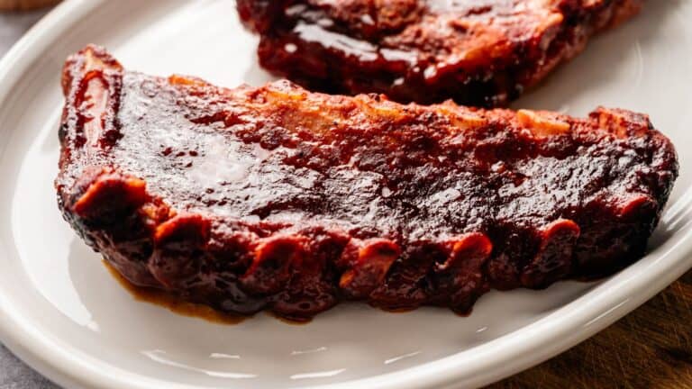 A close-up of a barbecued rack of ribs covered in a glossy sauce, served on a white plate.