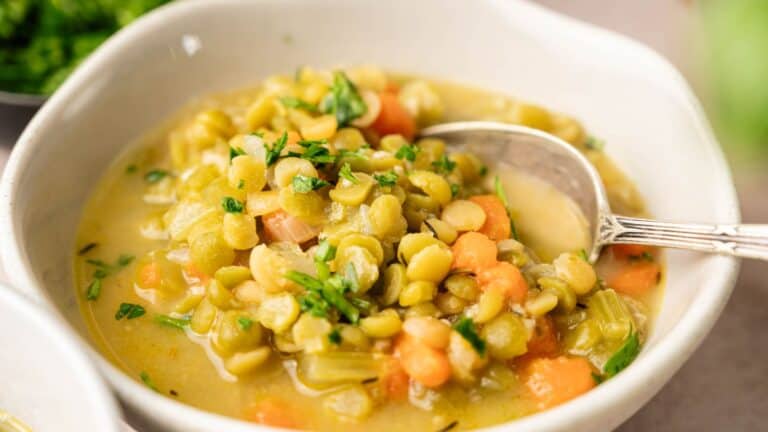 A bowl of split pea soup with chopped carrots, celery, and herbs, with a spoon resting in the bowl.