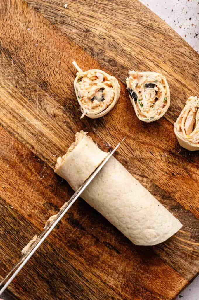 Knife cutting a rolled tortilla into 1-inch pinwheel slices