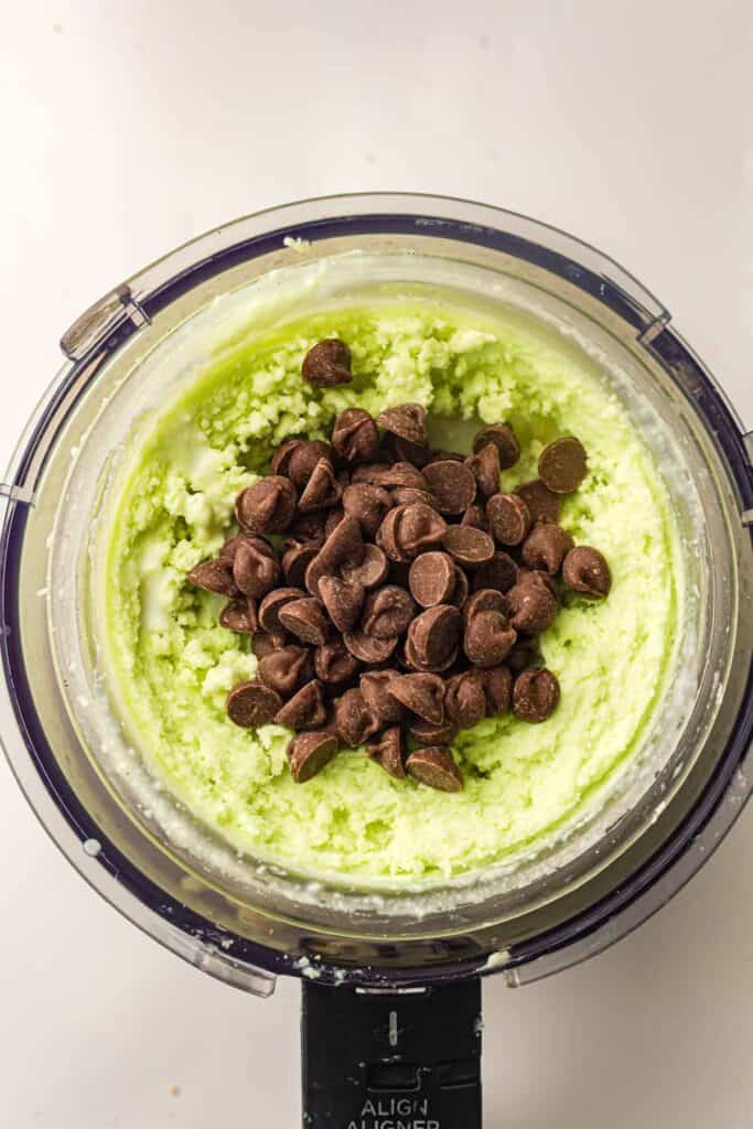Overhead view of chocolate chips sitting on smooth mint green ice cream before mixing in