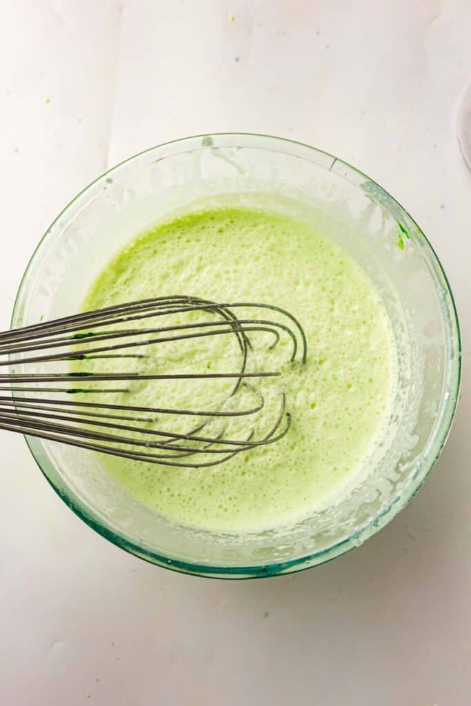 Whisk blending pale green mint ice cream base in a glass bowl