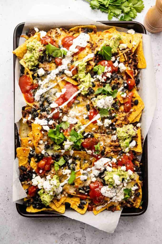 Sheet pan nachos topped with guacamole, salsa, and sour cream