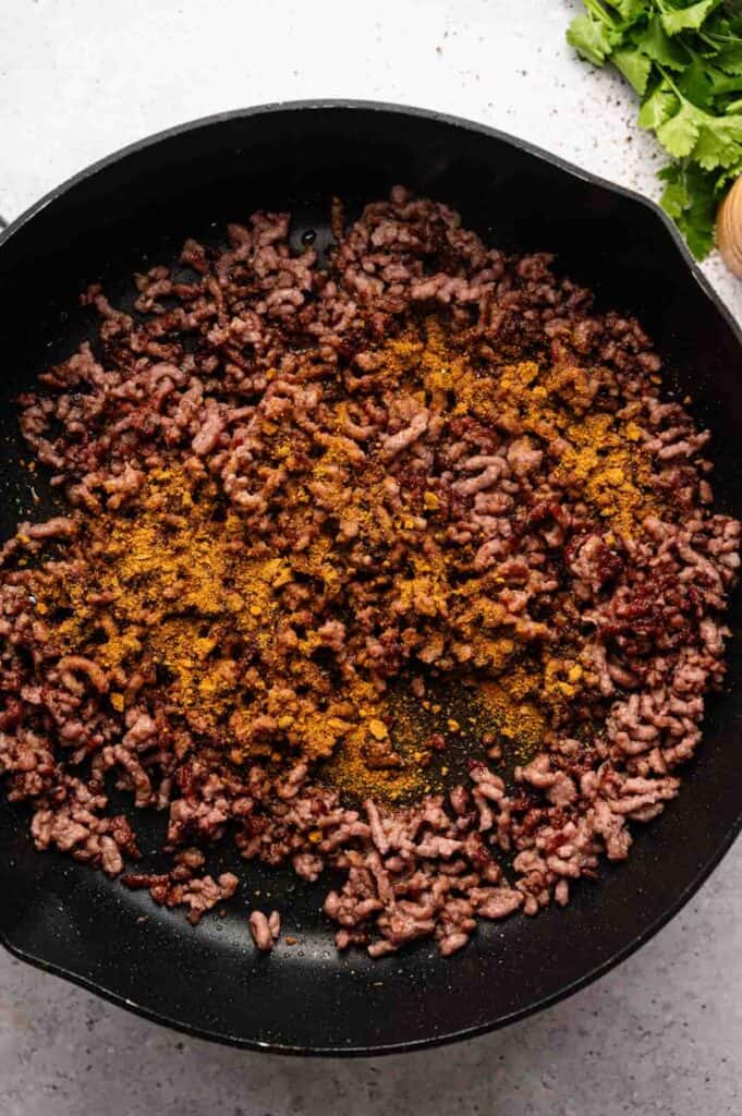 Ground beef browning in a skillet with chili powder