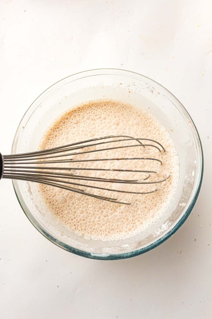 Overhead view of a whisk mixing milk, cream, and cocoa into a smooth chocolate base
