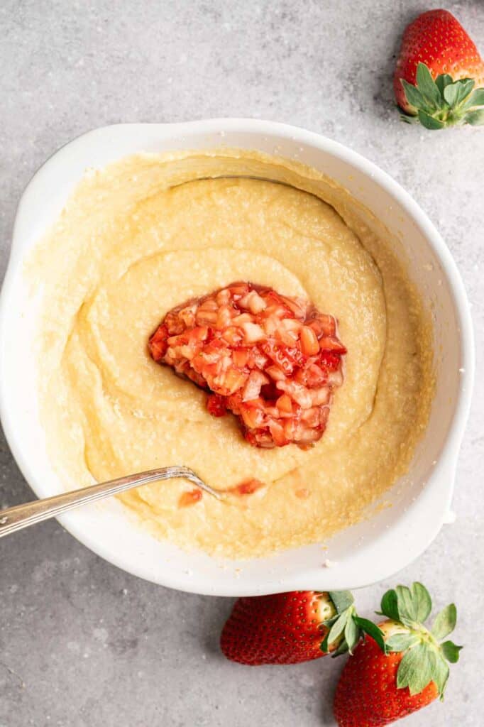Overhead view of chopped strawberries being folded into pale yellow batter