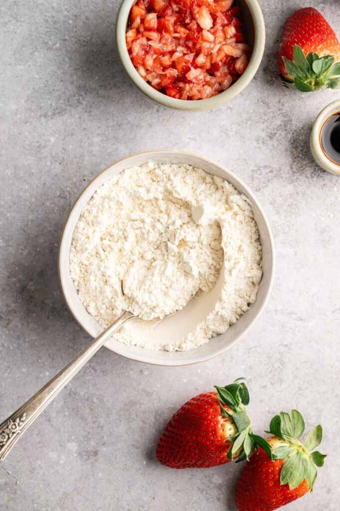 Overhead view of flour in a bowl surrounded by fresh strawberries