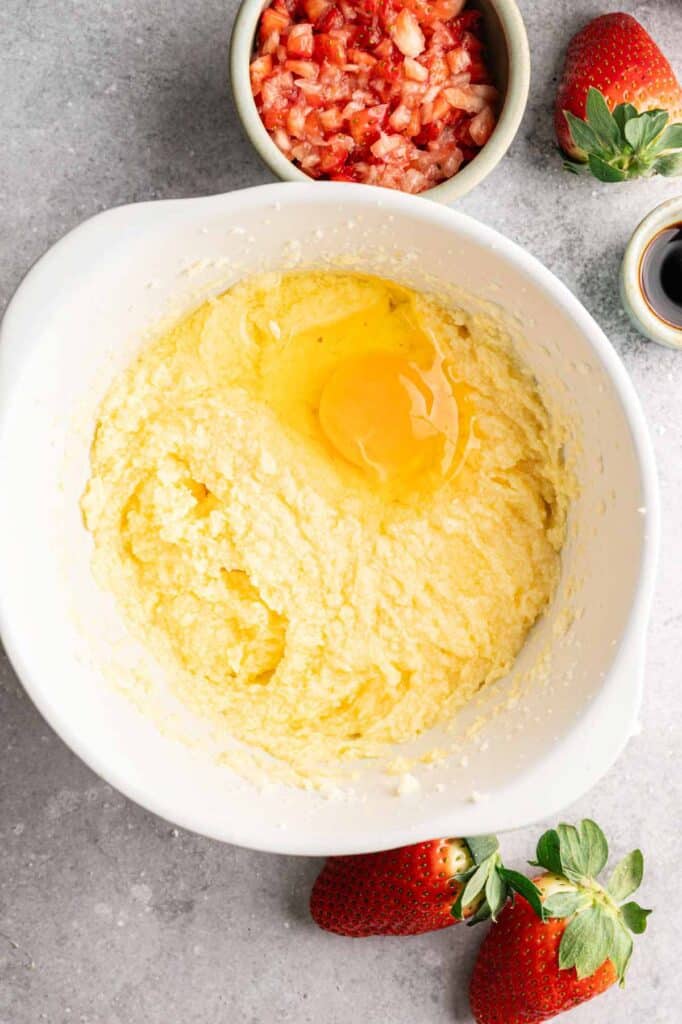 Overhead view of a raw egg cracked into fluffy butter and sugar