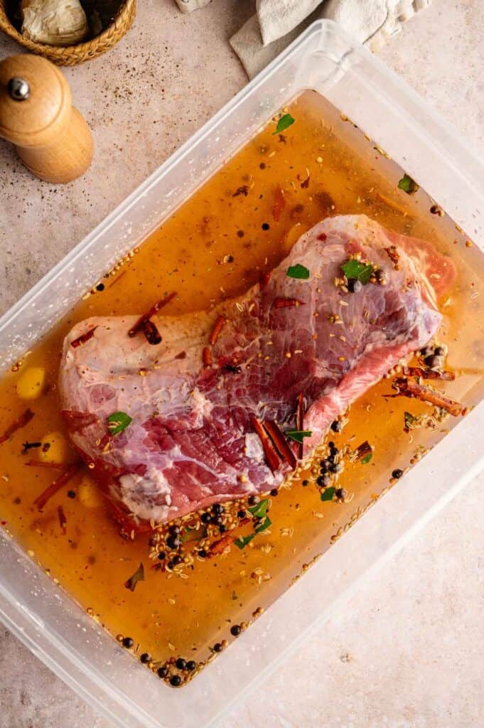 Raw brisket submerged in brine with peppercorns and bay leaves
