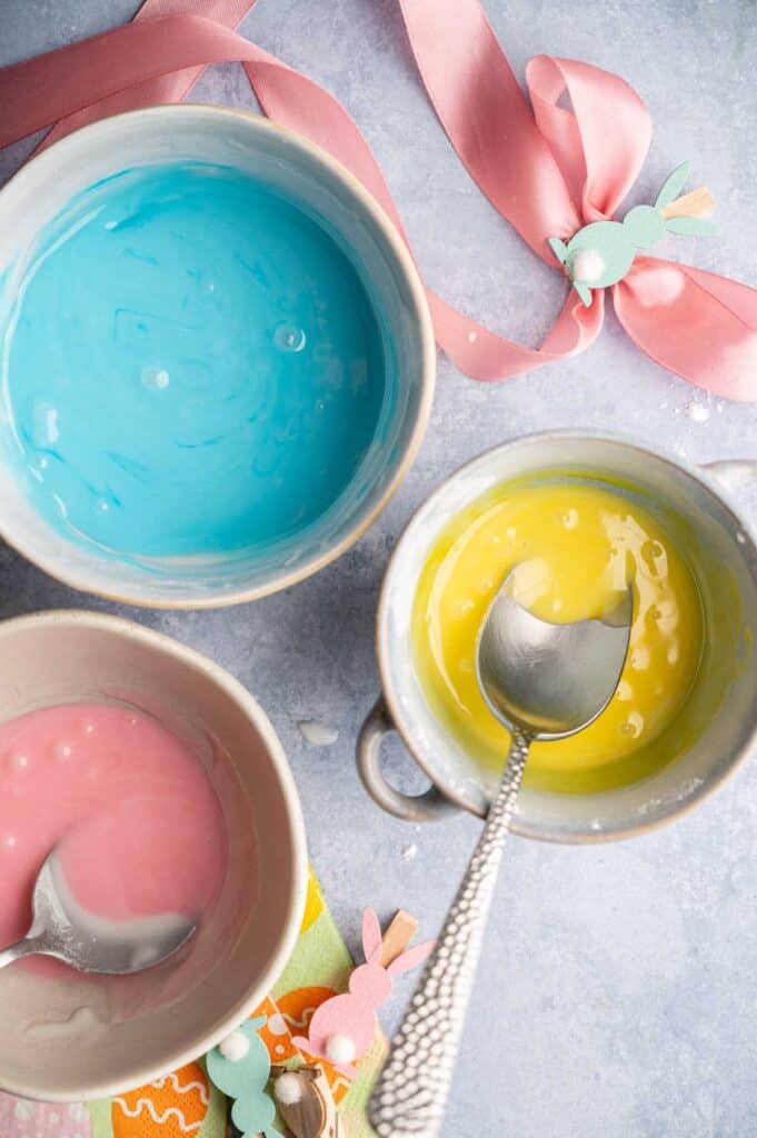 Blue, yellow, and pink icing mixed in separate bowls for decorating cookies