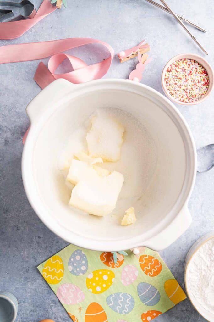 Overhead view of softened butter and sugar ready for creaming, with pastel ribbon and sprinkles nearby