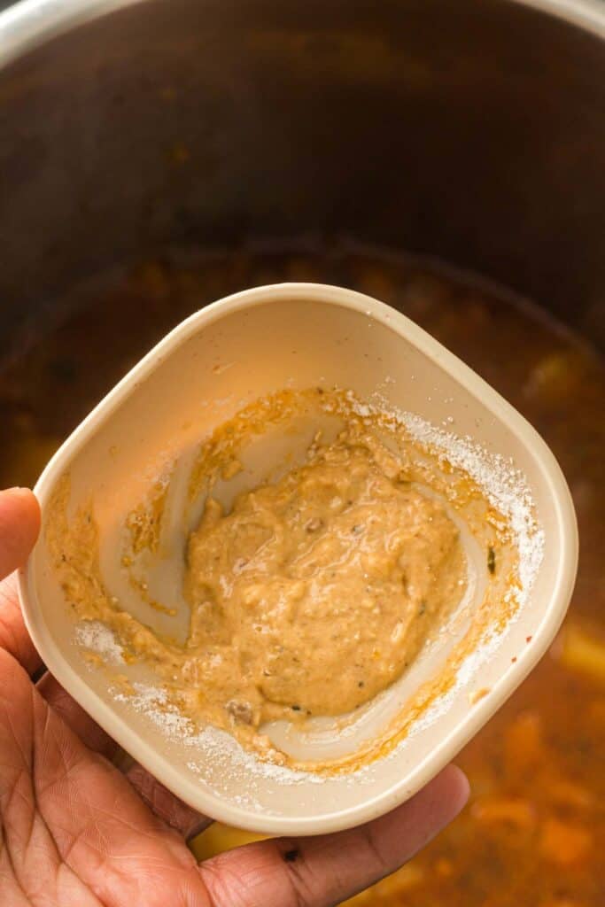 Close-up of a cornstarch slurry held over a pot of beef stew