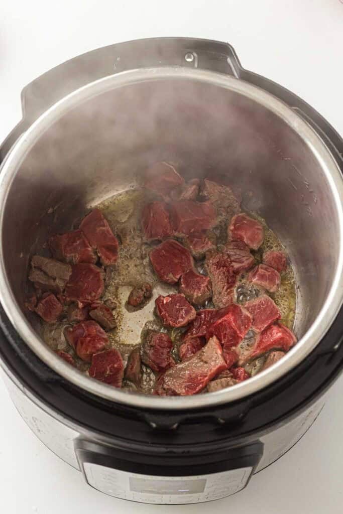 Overhead view of raw beef chunks searing in a pressure cooker