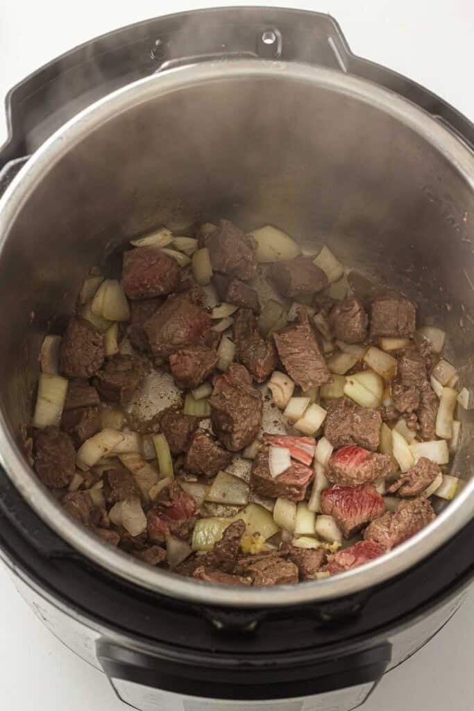 Overhead view of seared beef chunks mixed with softened onion