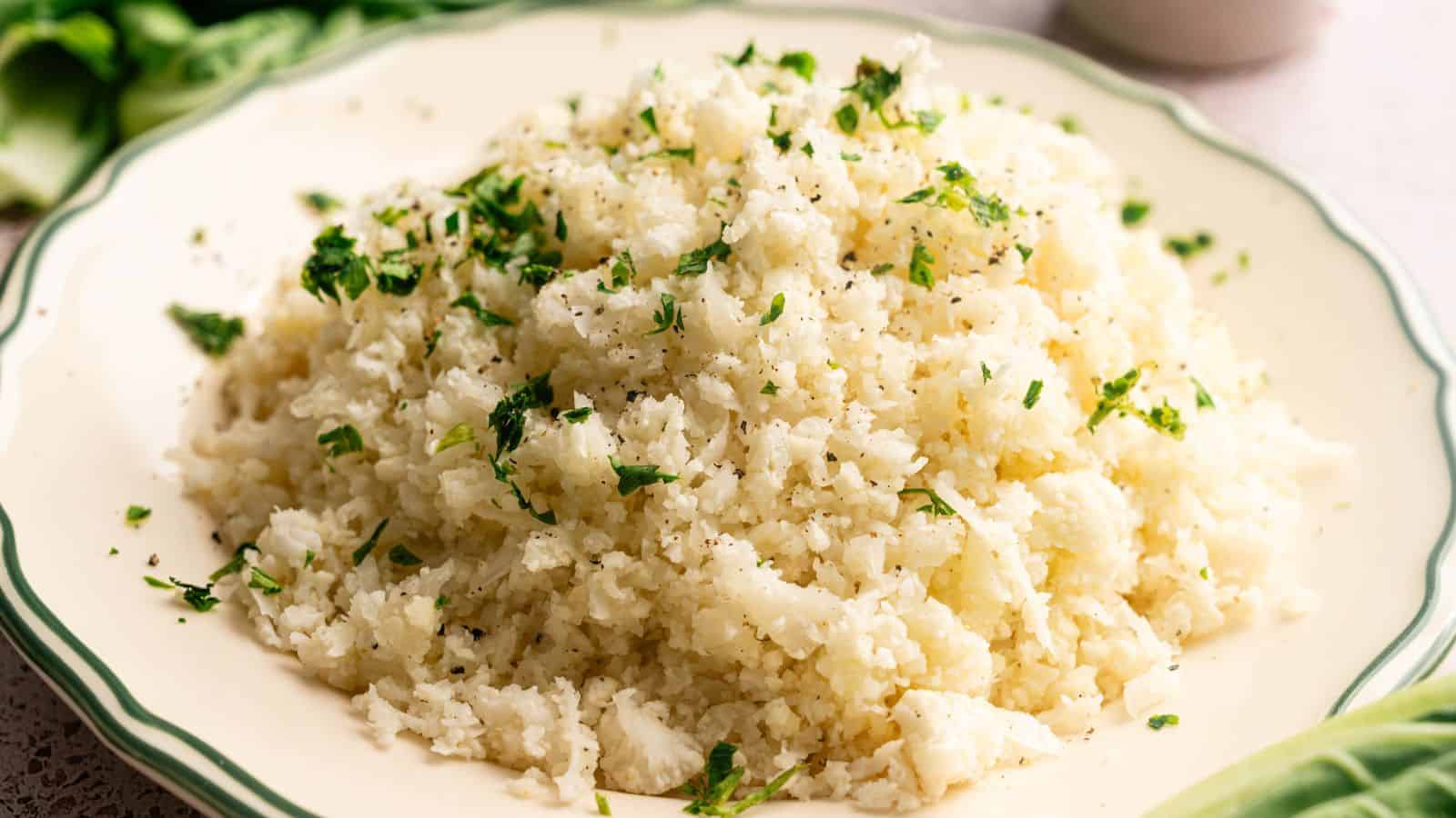 A plate of cauliflower rice garnished with chopped parsley and black pepper.