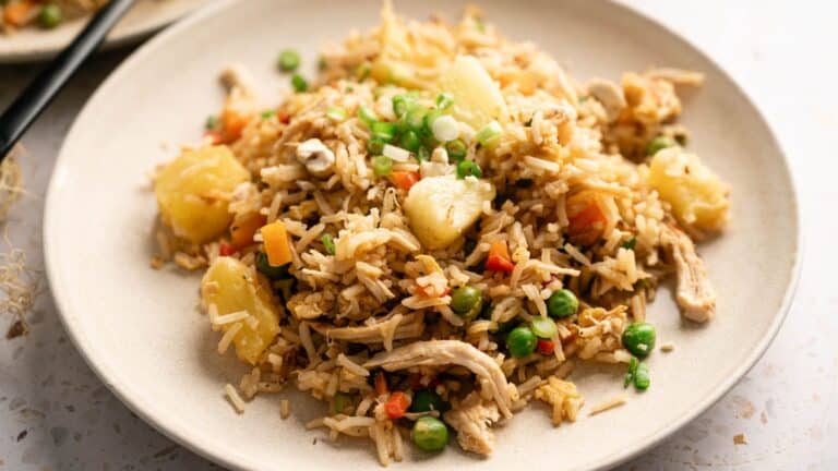 A plate of fried rice with pieces of pineapple, peas, carrots, shredded chicken, and green onions.
