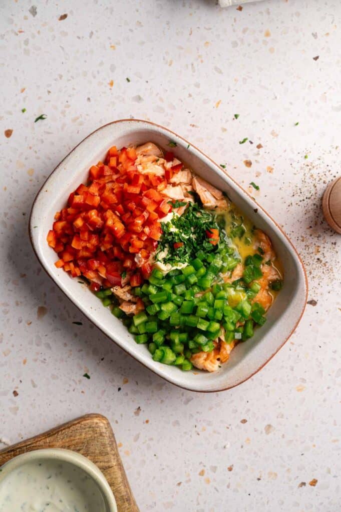 Flaked salmon topped with diced peppers, egg, and herbs in a dish