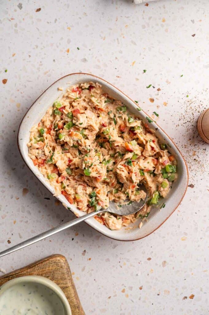 Salmon croquette mixture stirred together with peppers and herbs in a dish