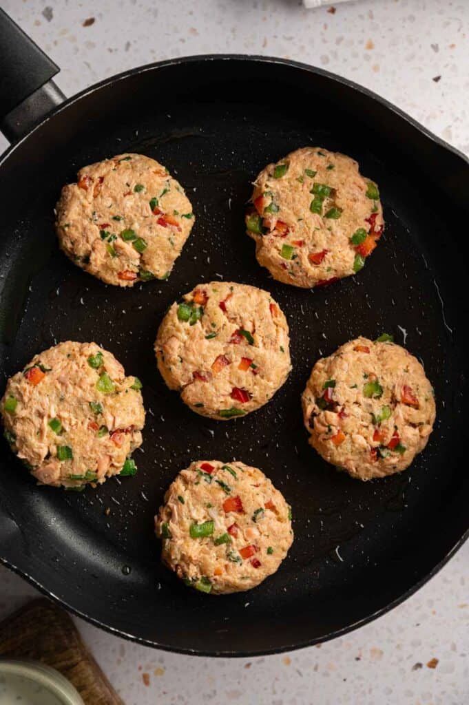 Raw salmon croquettes arranged in a black skillet before cooking