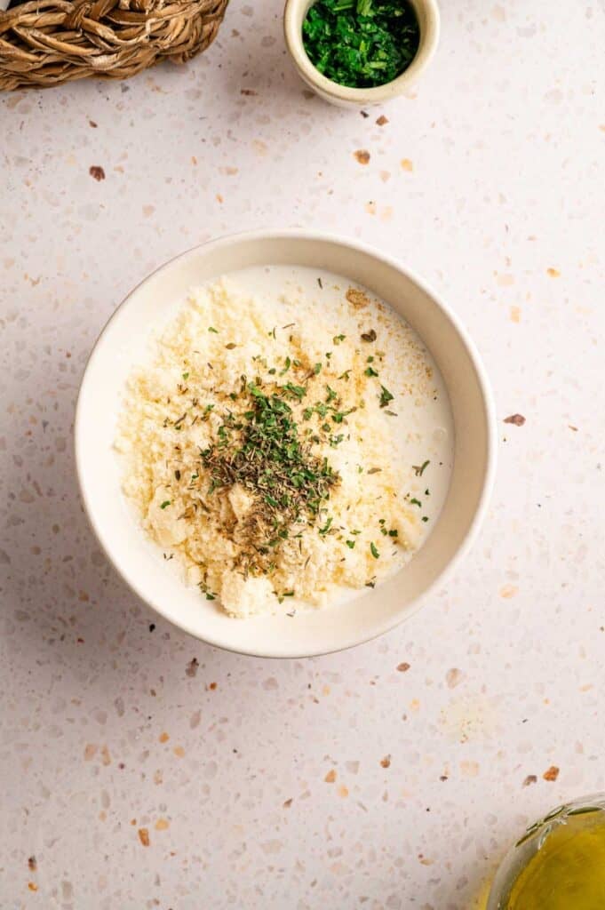 Overhead view of garlic Parmesan sauce ingredients topped with fresh herbs