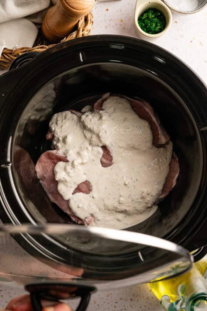 Creamy garlic Parmesan sauce poured over raw pork chops in a slow cooker