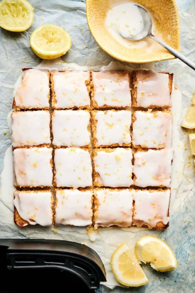 Sliced lemon brownies drizzled with lemon glaze, surrounded by fresh lemon wedges