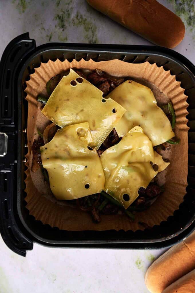 Provolone cheese slices laid over steak and pepper filling in the air fryer basket