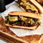 Three air fryer philly cheesesteak sandwiches filled with thinly sliced beef, melted cheese, and sautéed green peppers and onions, resting on white parchment paper over a baking sheet.