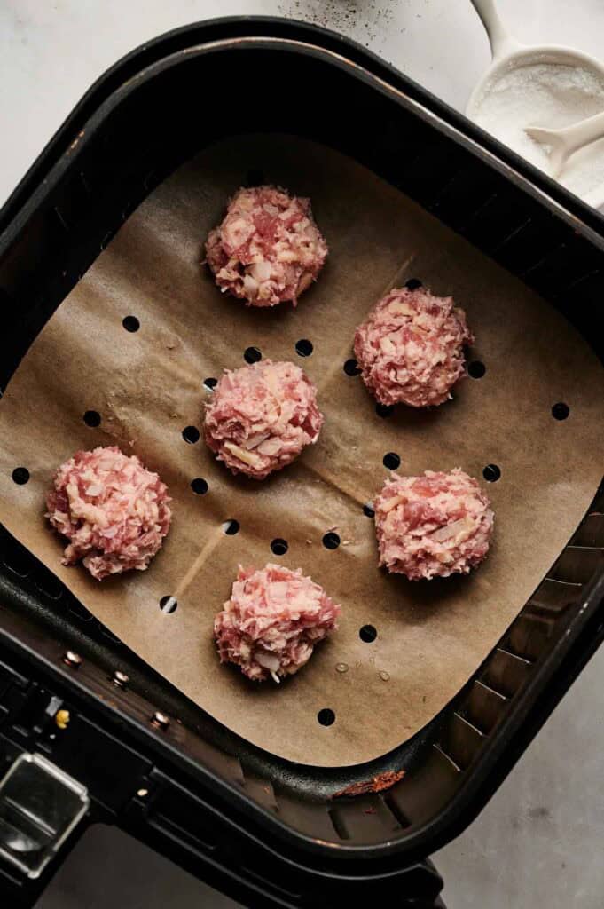 Raw sausage balls portioned in the air fryer basket before cooking