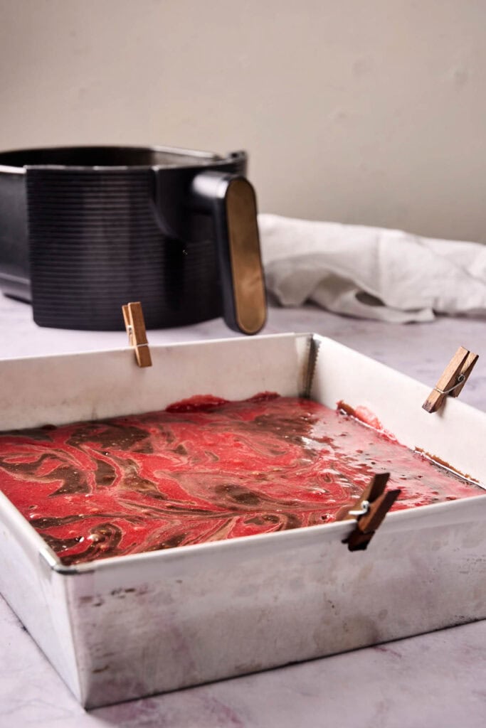 Unbaked chocolate strawberry swirl brownie batter in a square pan set in front of the air fryer