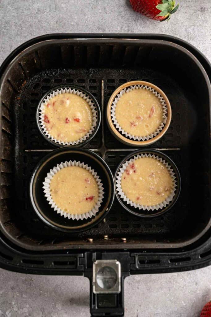 Unbaked strawberry cupcake batter with visible fruit pieces in liners set inside the air fryer