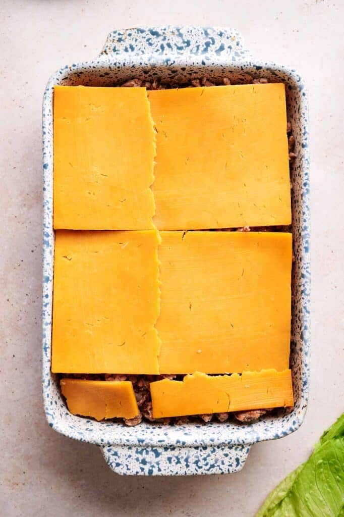 Sliced cheese layered over cooked ground beef on slider buns in a rectangular baking dish for Air Fryer Big Mac sliders.