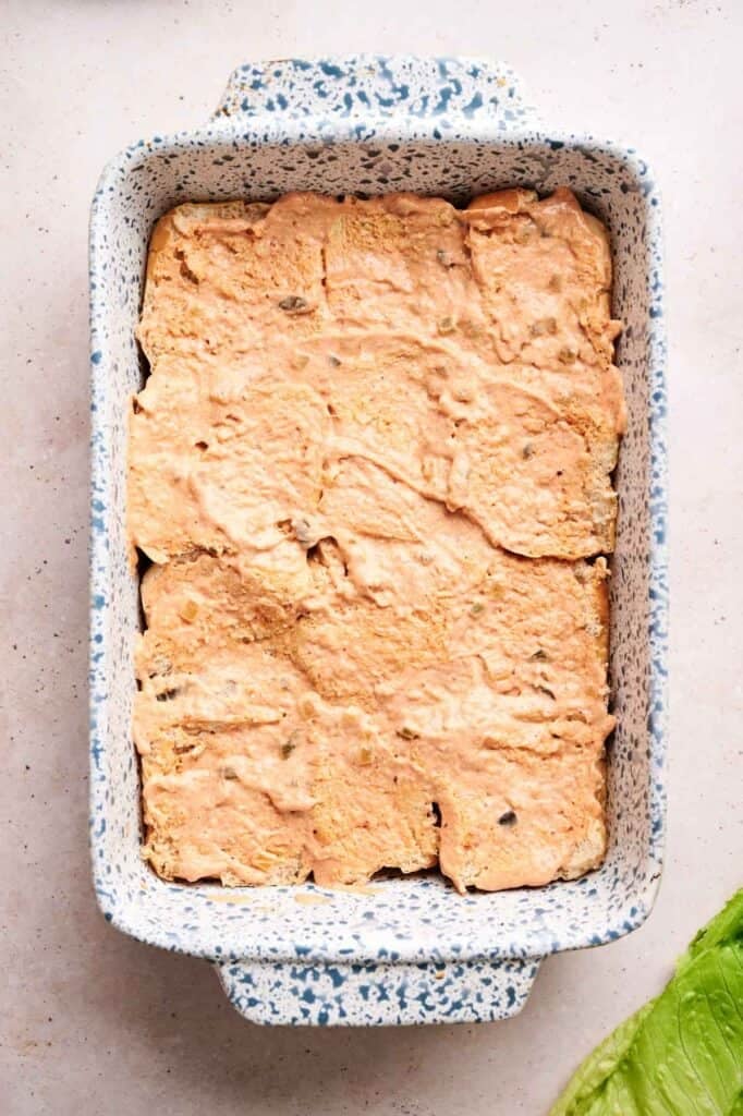Slider bun&nbsp;spread generously with homemade Big Mac sauce, arranged in a blue and white speckled rectangular baking dish, viewed from above.